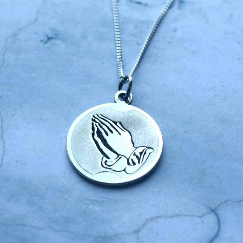 20 mm silver disc with praying hands image engraved on.  This pendant can be ordered alone or with a 45 cm curb chain included.